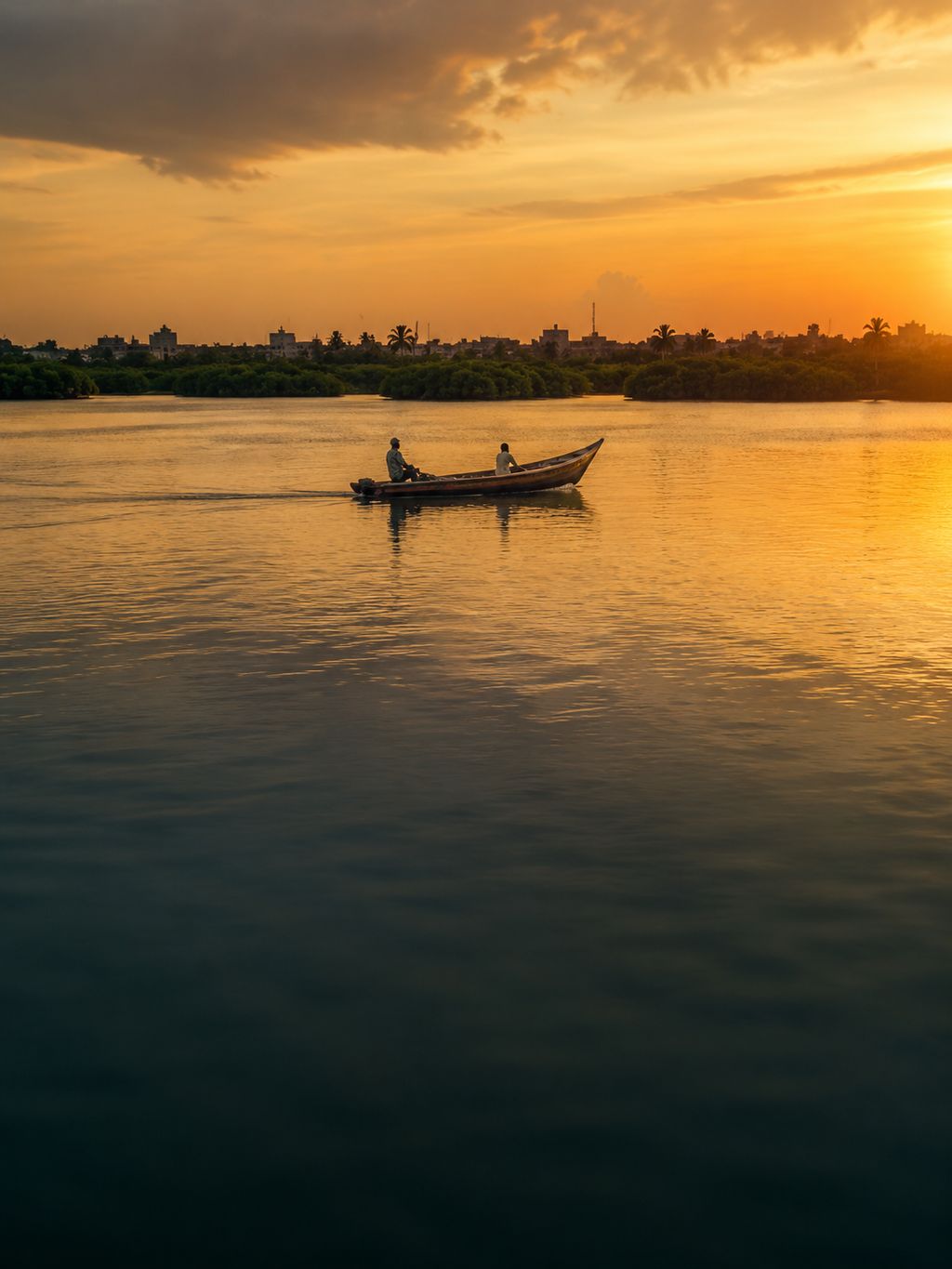 Une vedette remonte la lagune à l'heure dorée, la ville en silhouette derrière la mangrove.