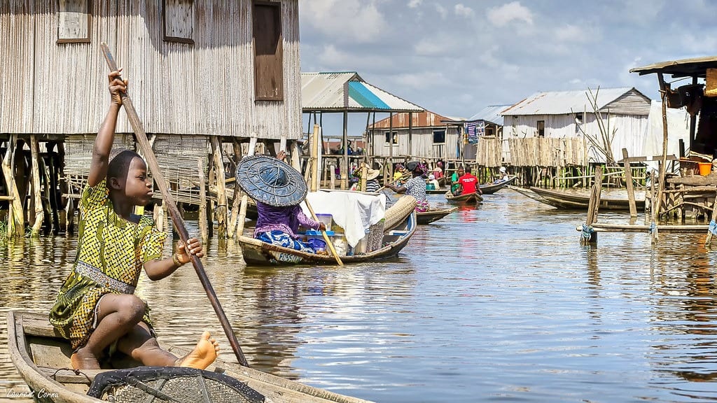 Un enfant pagaie debout dans une pirogue devant les maisons sur pilotis de Ganvié, au milieu du marché flottant.