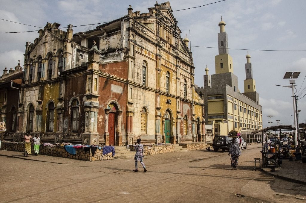 Une rue de Porto-Novo : maison afro-brésilienne aux couleurs passées et minarets de la grande mosquée.