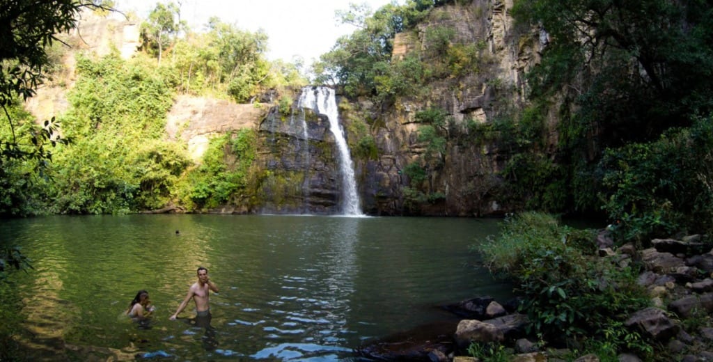 Deux baigneurs dans le bassin vert de la cascade de Tanougou, au pied de la chute.
